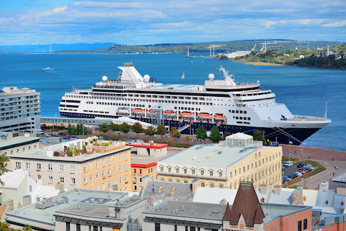 Cruise ship in river in Quebec City with blue sky and historical buildings.